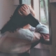 Woman at a window appearing distressed, holding her head, symbolizing emotional turmoil associated with BPD and emotional dysregulation.