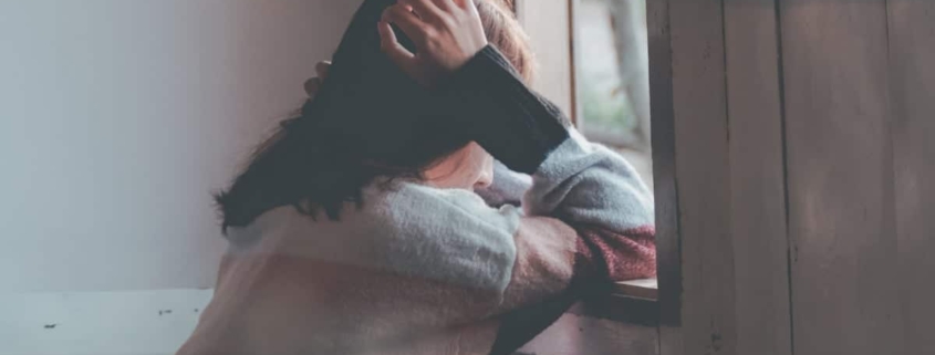 Woman at a window appearing distressed, holding her head, symbolizing emotional turmoil associated with BPD and emotional dysregulation.