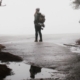 A woman standing alone on an empty road, with a reflection of herself in a puddle, symbolizing the disconnection and self-reflection experienced during a dissociative fugue state triggered by stress or trauma.