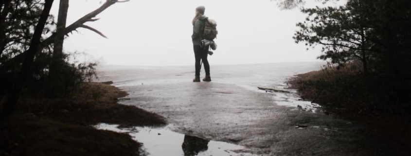 A woman standing alone on an empty road, with a reflection of herself in a puddle, symbolizing the disconnection and self-reflection experienced during a dissociative fugue state triggered by stress or trauma.