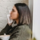 Woman sitting contemplatively by a white wall, pondering the potential benefits of CBD for anxiety.