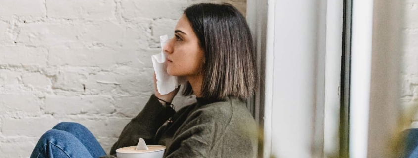 Woman sitting contemplatively by a white wall, pondering the potential benefits of CBD for anxiety.