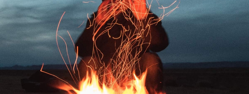 Man shielding his face from intense campfire flames, visually representing signs of anger issues.