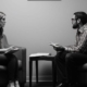 A man, seated comfortably, engaging in a counseling session with a compassionate woman. They discuss topics related to autism and mental health.