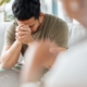 Man in military uniform during therapy session, head in hands, reflecting on PTSD causes and personal experiences.