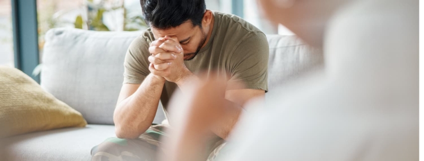 Man in military uniform during therapy session, head in hands, reflecting on PTSD causes and personal experiences.