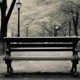 An image capturing the essence of anhedonia: a stark, empty bench in a park on a gloomy day, symbolizing loneliness and emotional numbness.