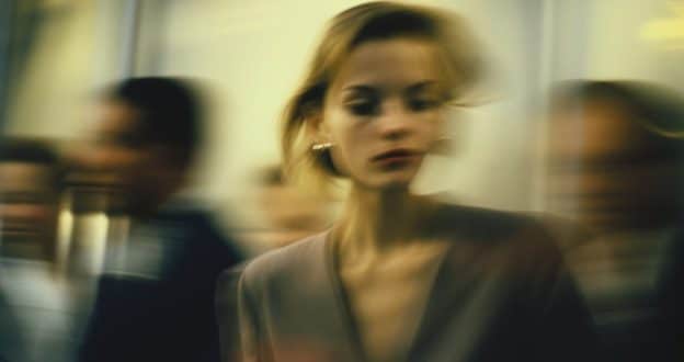 A woman in a blurry social setting with subtly distorted features, visually representing Body Dysmorphia Symptoms and the feeling of disconnection in social environments.
