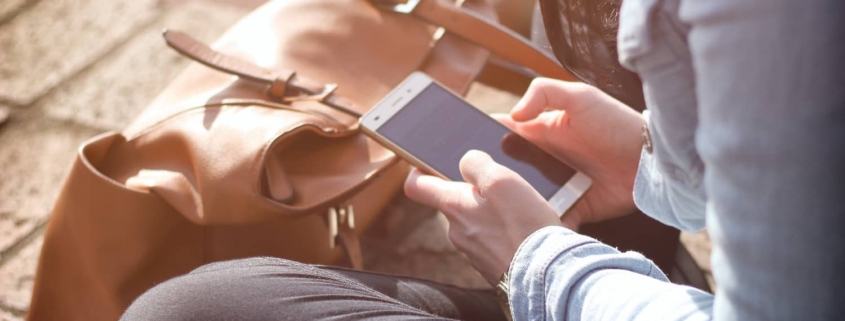 Anxious woman sitting on a sidewalk, intently looking at her cell phone, illustrating the concept of Nomophobia.