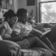 A couple sits closely on a couch, deeply engaged in reading an educational book about PTSD, highlighting a moment of mutual learning and understanding in their relationship.