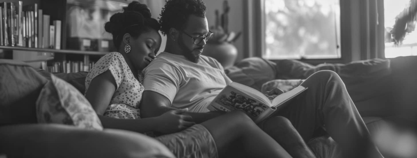 A couple sits closely on a couch, deeply engaged in reading an educational book about PTSD, highlighting a moment of mutual learning and understanding in their relationship.