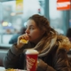 A woman with binge eating disorder sitting in a fast food restaurant, consuming a meal.